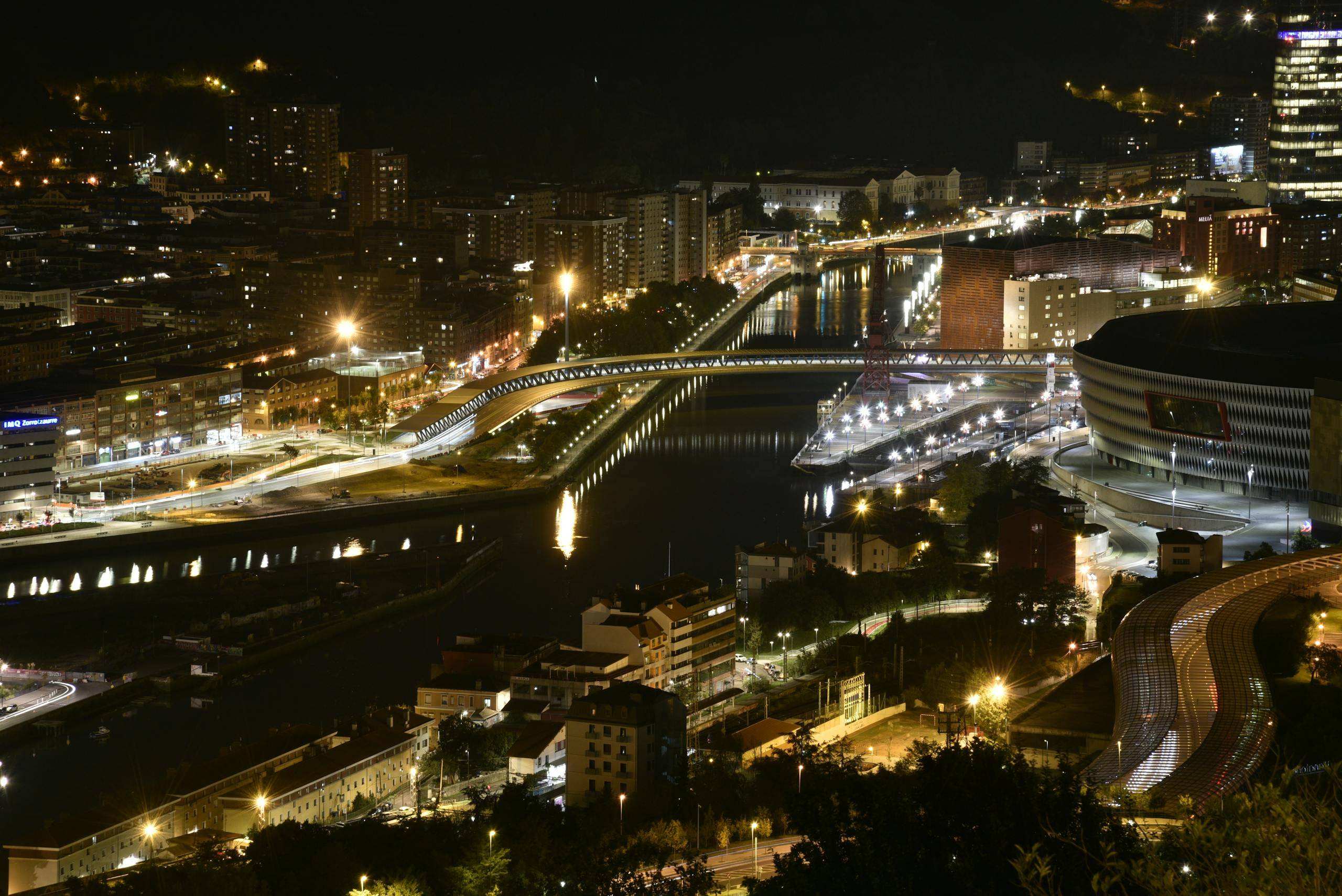 Panoramic view of a bustling city at night with glowing lights reflecting on the river.